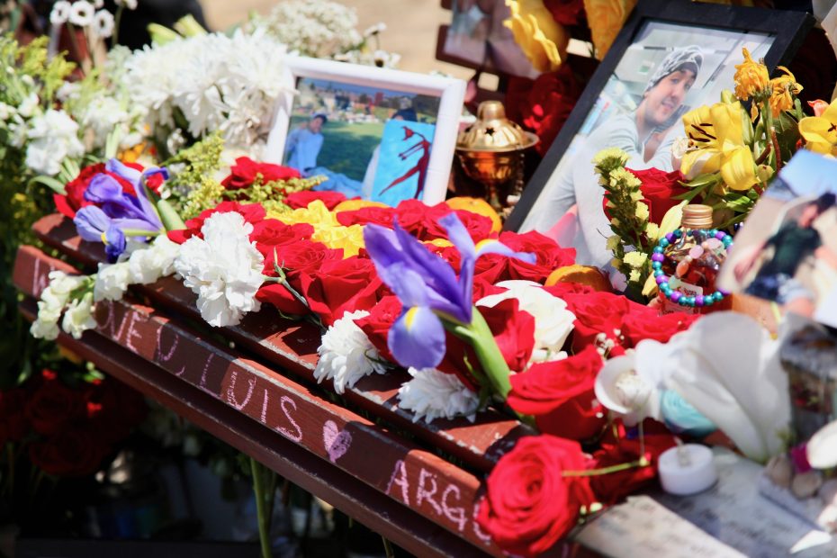 A memorial display featuring photos, colorful flowers, candles, and personal mementos including a sign with "LOVE U LUIS" written on it.