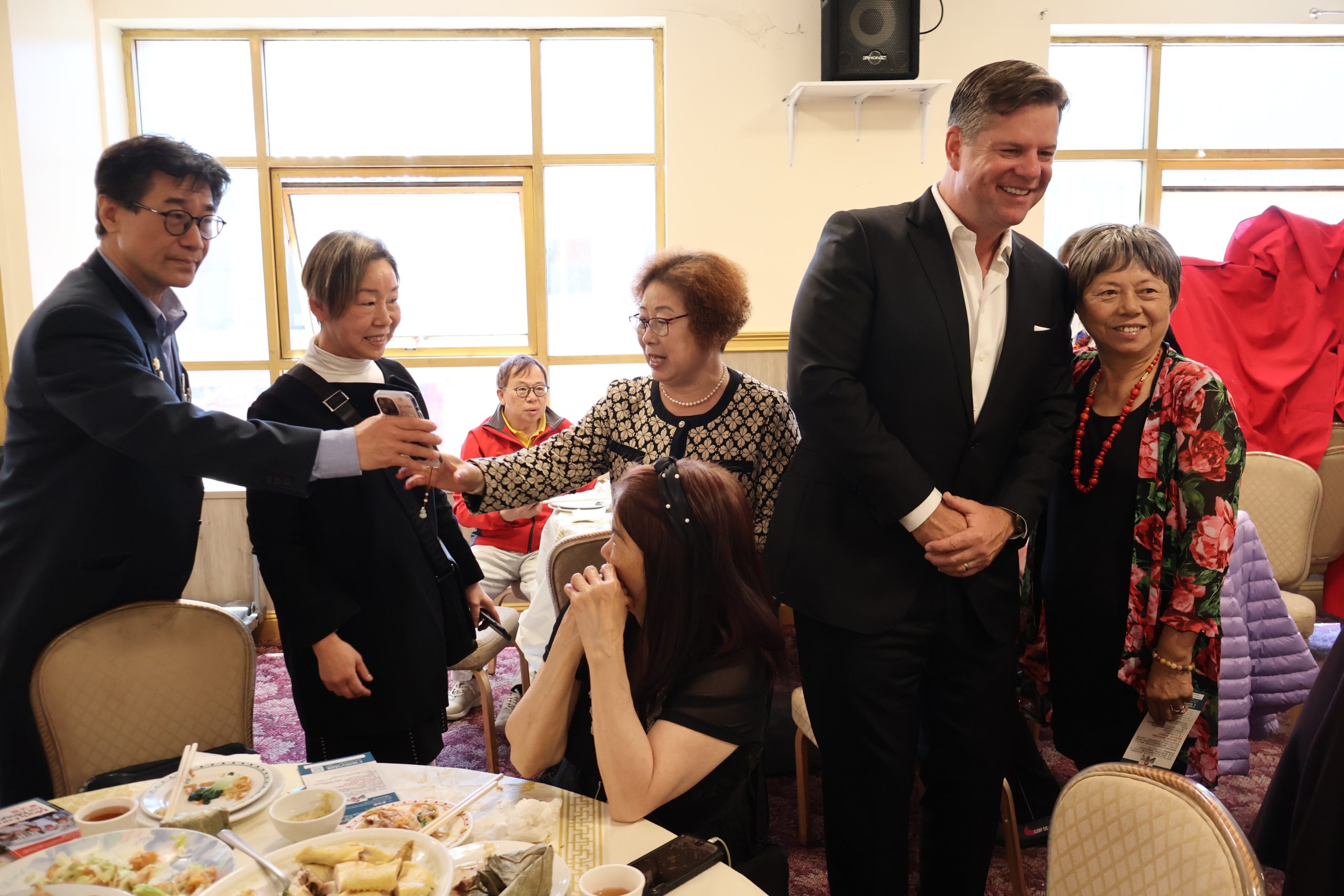 一群人站着，围坐在餐桌旁，桌上摆着一盘盘食物。他们在互动，似乎在交谈，有些人还面带微笑。