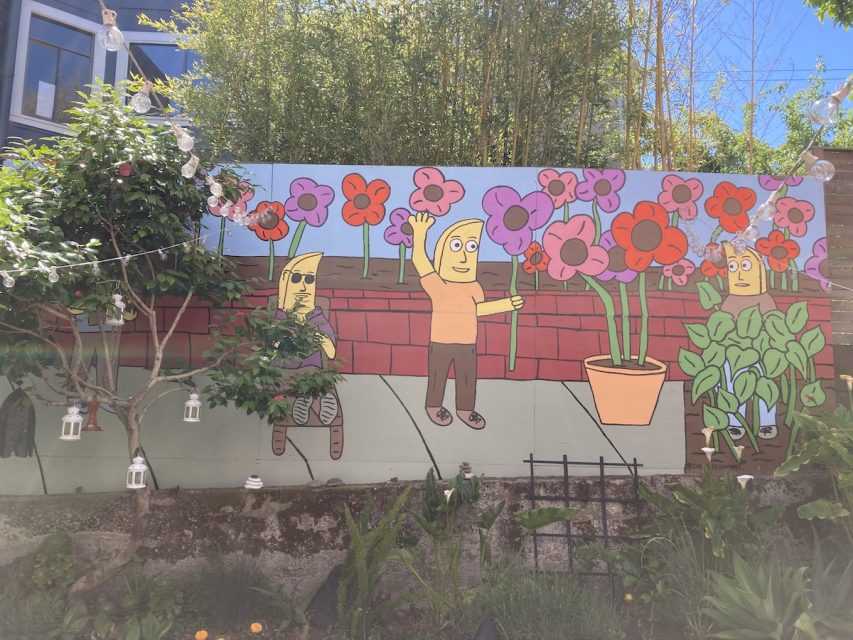 A mural depicting bananas in front of purple, orange and pink flowers.