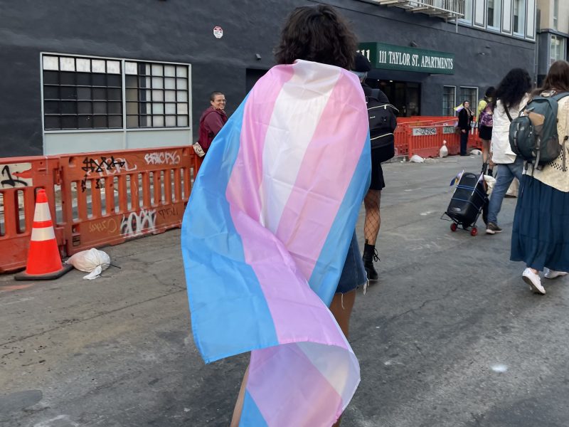 a person wears a trans flag as a cape