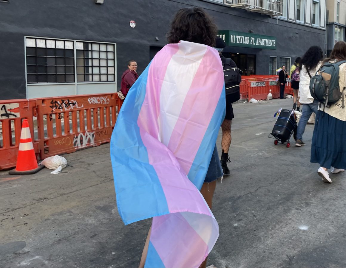 a person wears a trans flag as a cape