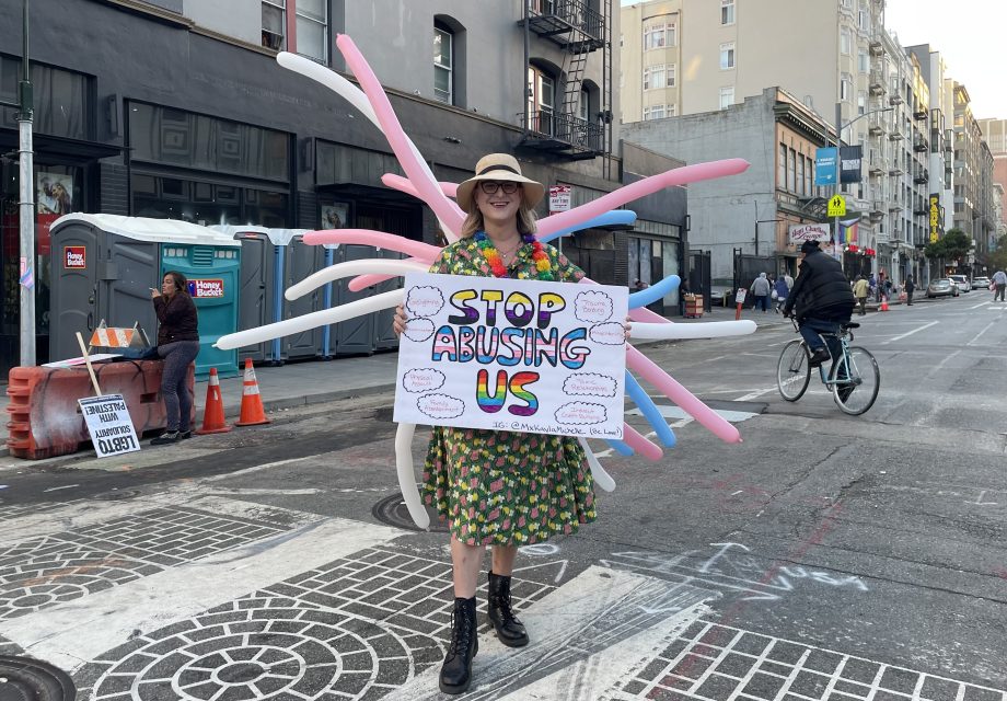 A woman with train of balloons poses with a sign in a street intersection. The sign says "Stop abusing us"