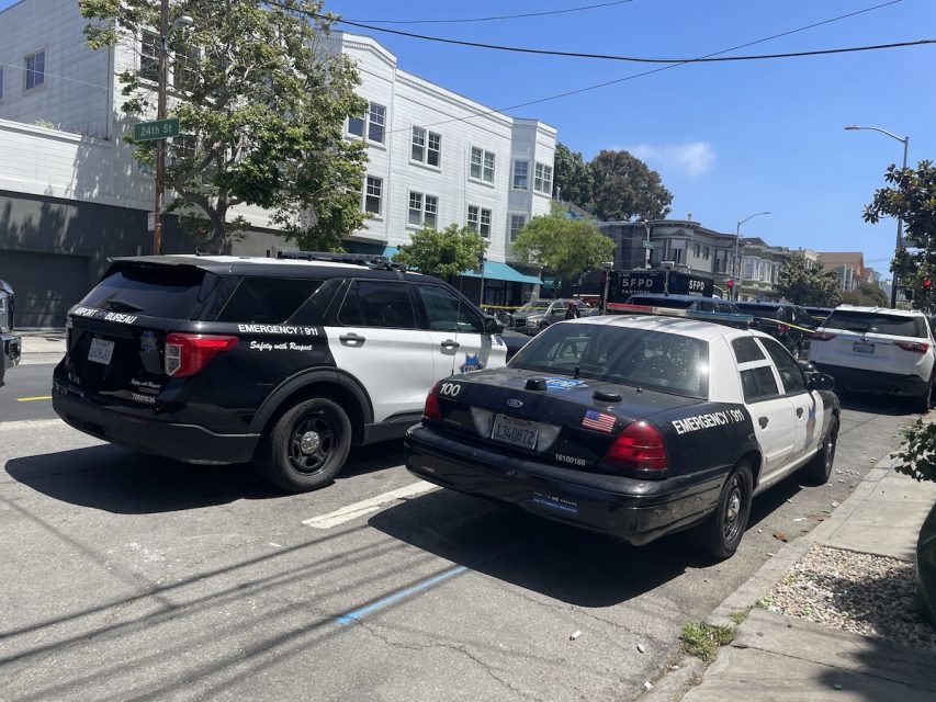 Two police vehicles, including a SWAT unit, are parked on a sunny city street near white buildings and trees. One is modern, black and white; the other is classic, black and white, with "Emergency 911" on both.