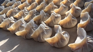A tray of uncooked dumplings is arranged in rows, with each dumpling folded and pinched at the top. The dough is pale and slightly translucent.