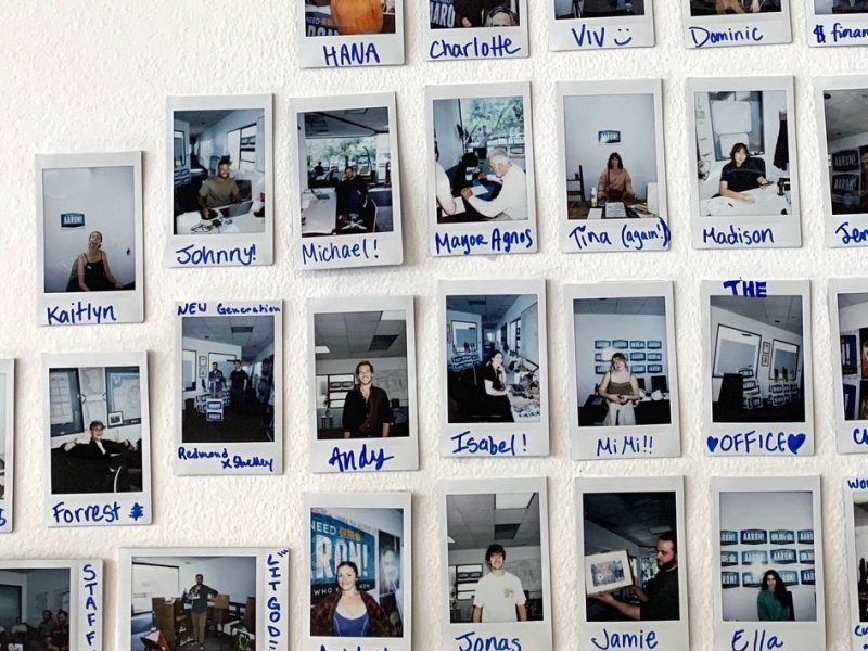 Wall display of Polaroid photos featuring various individuals in office settings, each labeled with handwritten names.