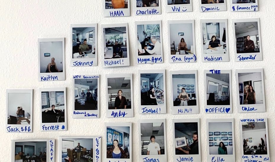 Wall display of Polaroid photos featuring various individuals in office settings, each labeled with handwritten names.