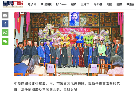 A group of people posing for a photo in front of a colorful stage with a portrait above them. The setting features ornate decorations and several vibrant, costumed figures.