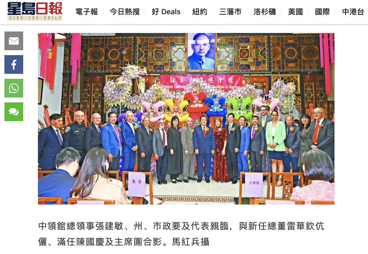 A group of people posing for a photo in front of a colorful stage with a portrait above them. The setting features ornate decorations and several vibrant, costumed figures.