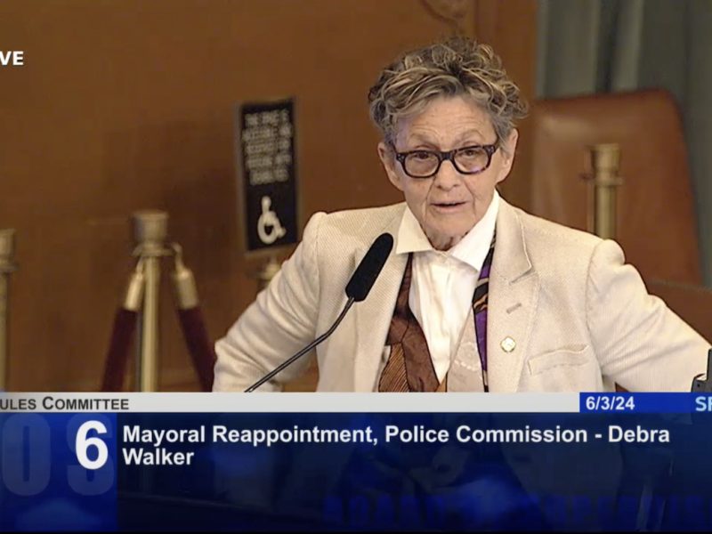 An individual is speaking at a podium during the Rules Committee meeting shown on SFGov TV. The agenda item displayed is number 6: Mayoral Reappointment, Police Commission - Debra Walker.