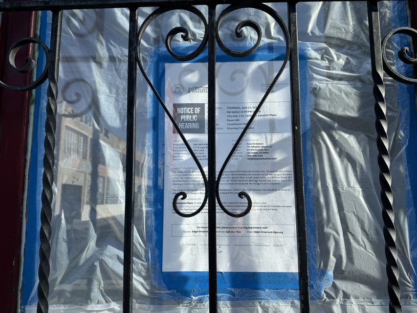A "Notice of Public Hearing" sign taped to a window, partially obscured by bars and reflective plastic covering.