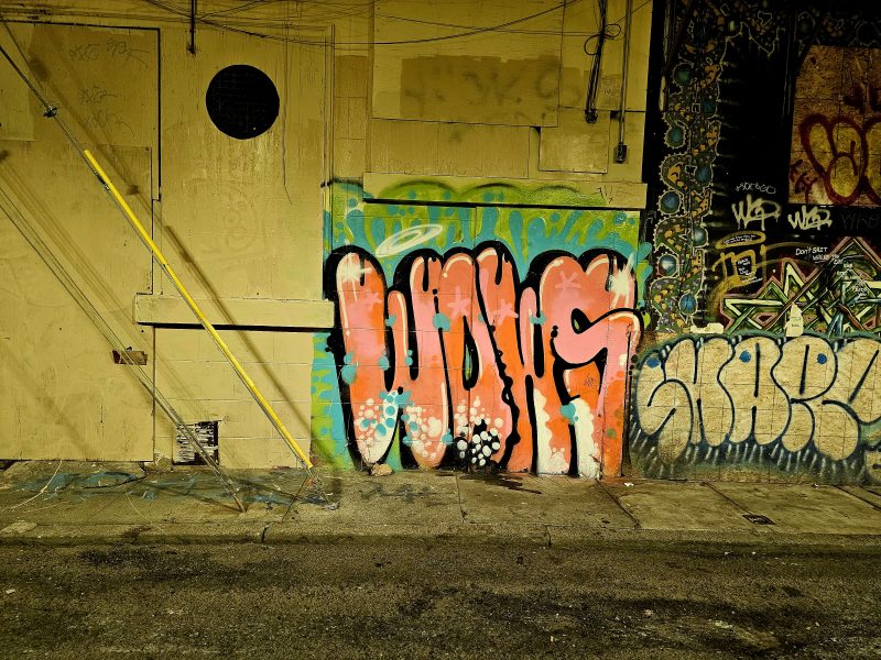 A wall with colorful graffiti art, including the word "WOWS" in large, bold letters. The background features various patterns and tags in assorted styles and colors.