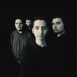 A black and white photo of four men standing in a dark environment, with one man in the foreground and three men in the background.