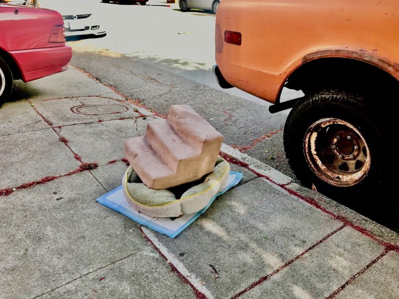 Two cars are parked on a street near a sidewalk, where a small set of beige stairs with protective padding snaps into view.