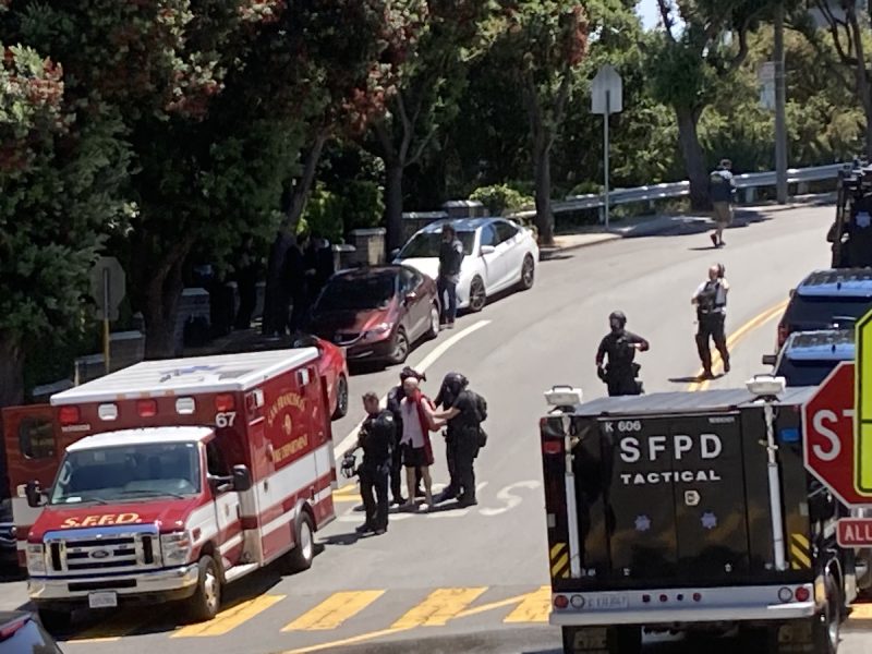 A suspect in a white shirt and dark shorts being escorted in handcuffs by police officers after he shot at them during an eviction