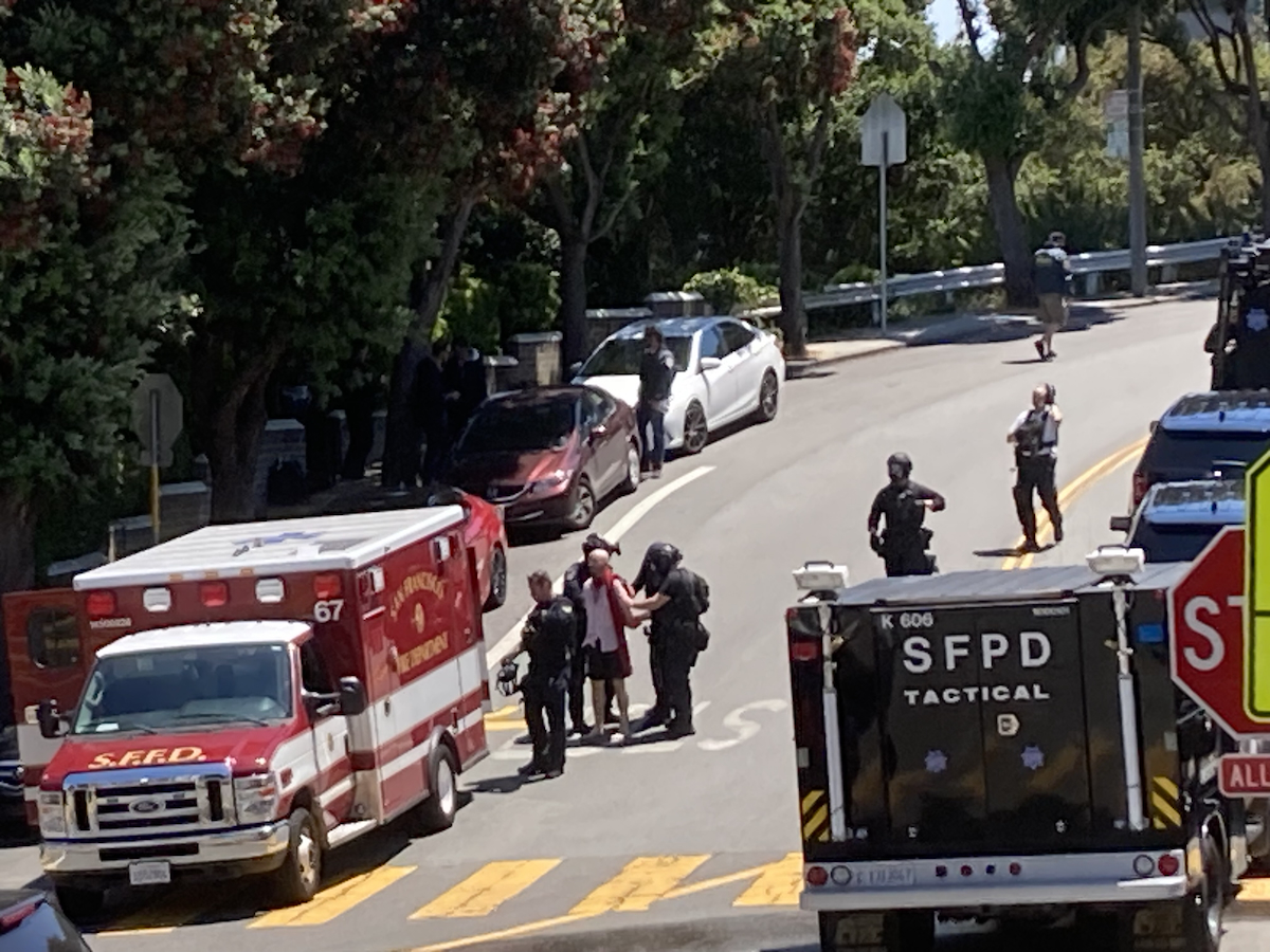 A suspect in a white shirt and dark shorts being escorted in handcuffs by police officers after he shot at them during an eviction
