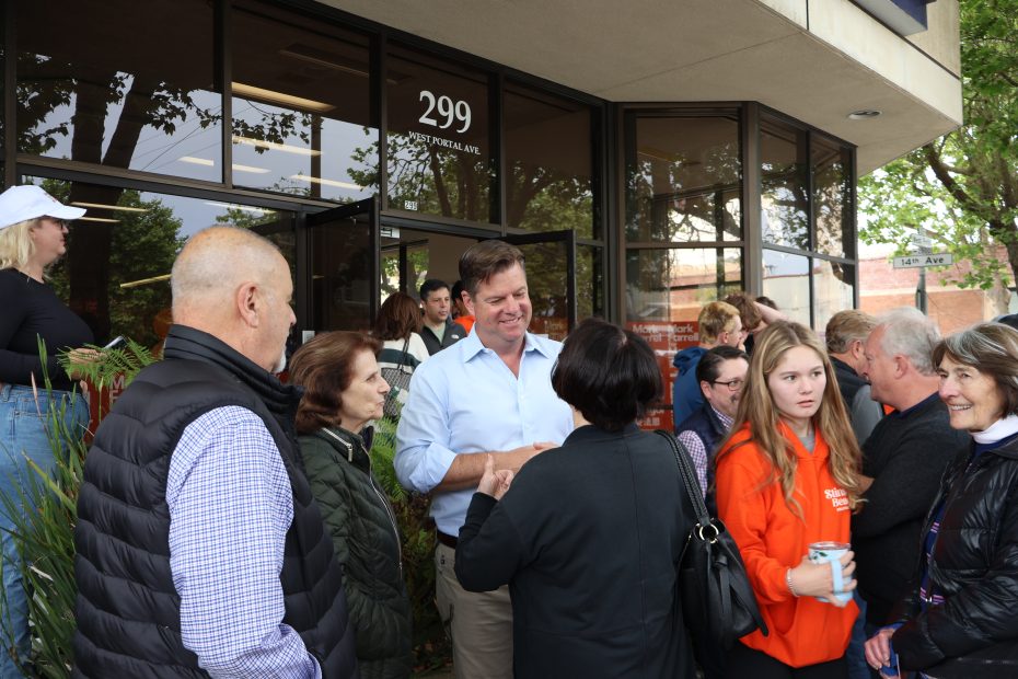 一群人，包括一名身穿淺藍色襯衫的男子，聚集在一棟寫著「299」的大樓外。有些人在聊天，有些人則在觀看。