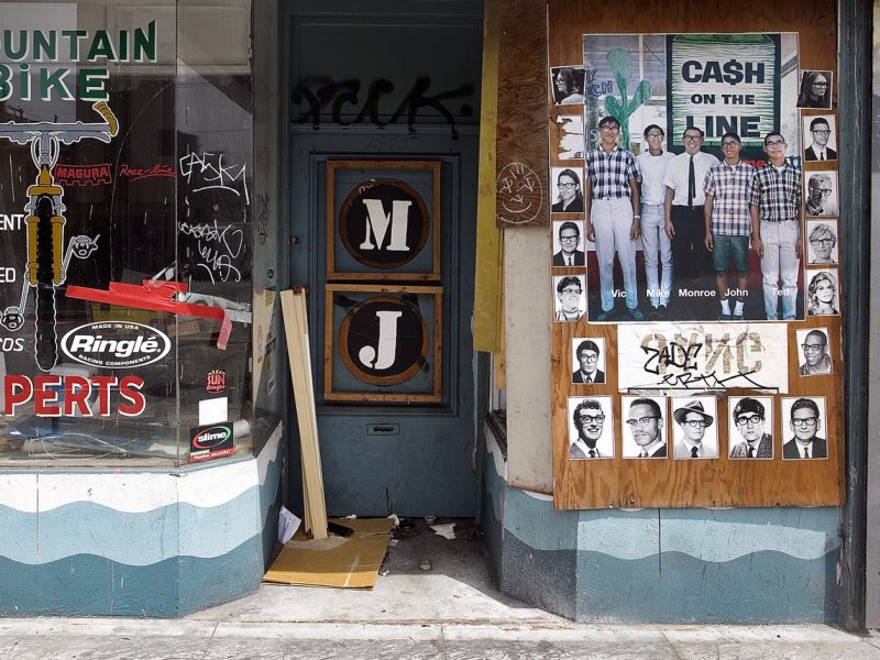 A storefront with displayed signs, including "Mountain Bike Experts" and a poster showing multiple headshots under the text "Cash on the Line." The entrance area is cluttered.