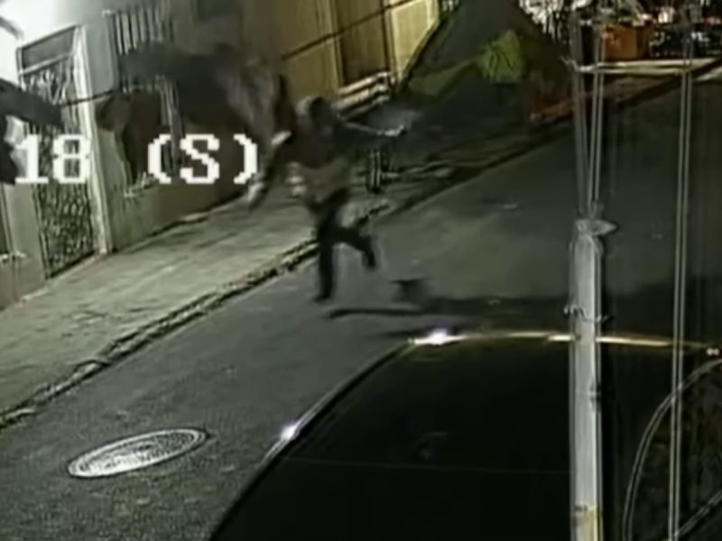 Surveillance footage showing a person running on a dimly lit street at night, near parked cars and buildings.