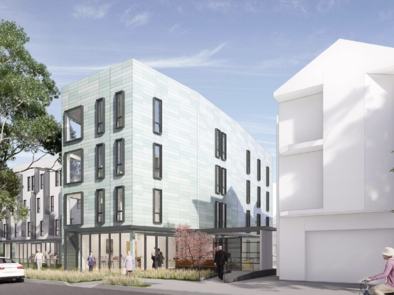 Modern multi-story building with large windows and greenish exterior at 3333 Mission. People walk and cycle nearby, with trees and a car in the foreground. Adjoining white building on the right.