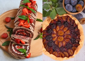 A chocolate Swiss roll cake garnished with strawberries and mint leaves sits on a wooden platter next to a plum tart with a decorative crust, accompanied by fresh plums and green leaves.