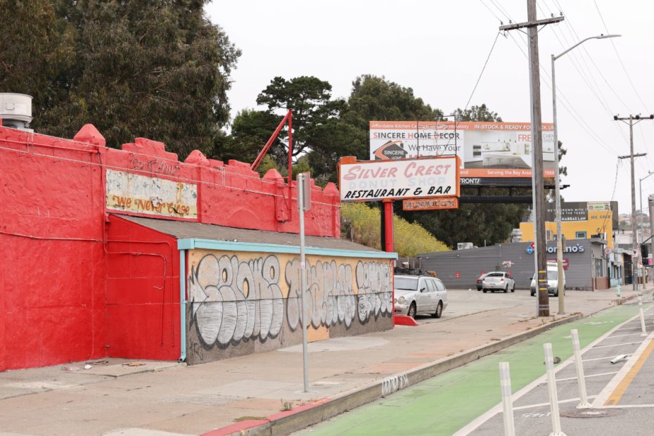 A bright red building with graffiti on the side and a sign reading "Silver Crest Restaurant & Bar." Several billboards and a Domino's Pizza can be seen in the background on a cloudy day.