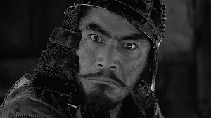 Black and white close-up of a man wearing traditional samurai armor and headgear, with a serious and intense expression on his face.