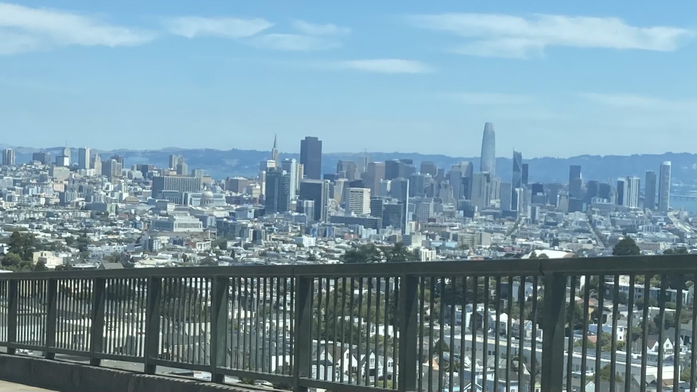 A clear daytime view of a city skyline with a variety of tall buildings and a bridge railing in the foreground.