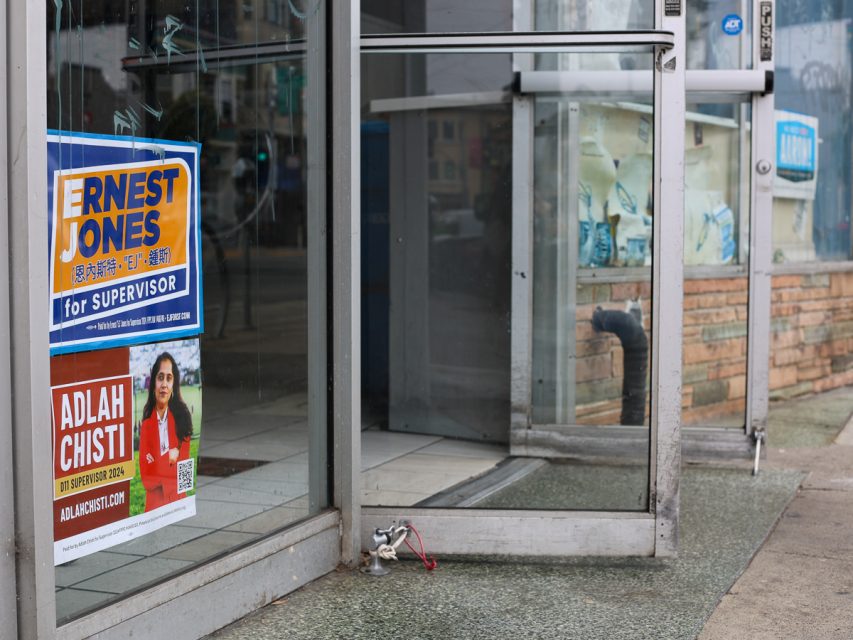 當地參事候選人 Ernest Jones 和 Adlah Chisti 的競選海報展示在一個店面的玻璃門上，附近地上有一個金屬纜鎖。