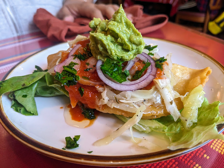 A plated dish with shredded chicken, sliced onions, guacamole, tomato sauce, and herbs on a bed of lettuce, set on a red tablecloth in a restaurant setting. at Antigua Guatemala.