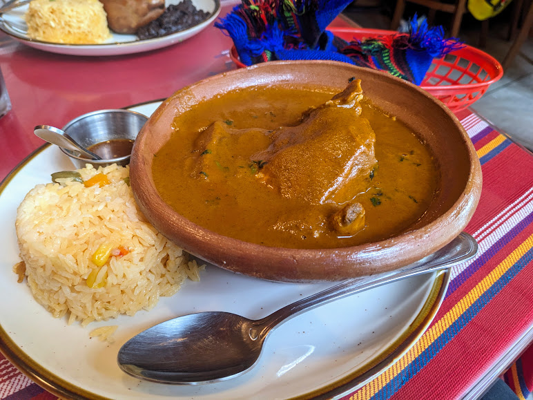 A plate with yellow rice and a bowl of curry, accompanied by a spoon, on a colorful table. at Antigua Guatemala