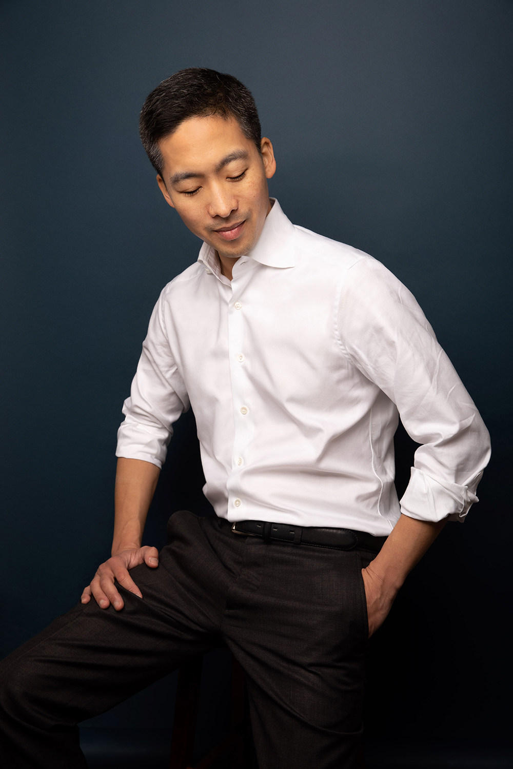 A person in a white dress shirt and dark pants stands against a dark blue background, looking down with one hand in their pocket, reminiscent of an attendee at the SF Zine Fest.