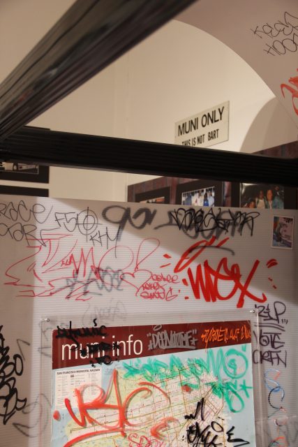 Graffiti-covered wall with a "muni info" map in an indoor space. A "MUNI ONLY" sign is visible above the wall.