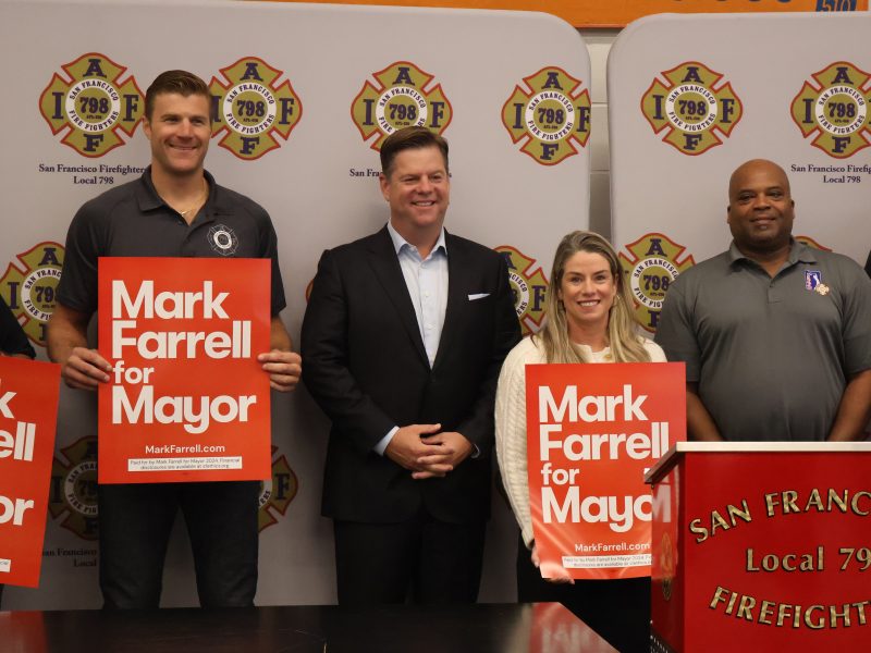 Four individuals stand together, with two holding "Mark Farrell for Mayor" signs. A podium with "San Francisco Firefighters Local 798" is in the foreground, and a backdrop features the same organization's logo.