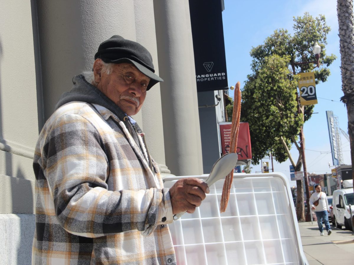 Raymundo Jimenez poses with one of his homemade churros at the intersection of 21st and Mission streets on Friday Aug. 9, 2024. Photo by Oscar Palma.