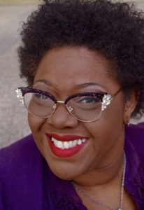 Person wearing glasses with decorative frames, a purple top, and red lipstick, smiling at the camera.