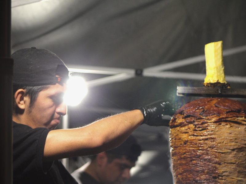 Daniel Contreras slicing some meat off a trompo to make al pastor tacos at "El gran trompo regio" on Saturday Aug. 10, 2024. Photo by Oscar Palma.