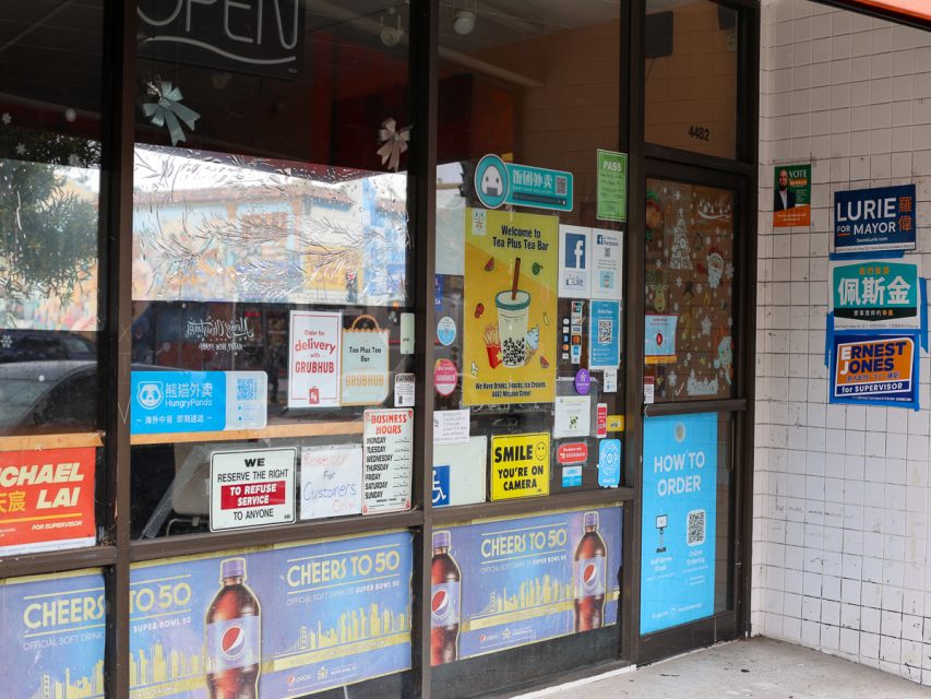 店面櫥窗被各種海報、標誌和廣告覆蓋，宣傳不同的服務、產品和當地政治候選人。