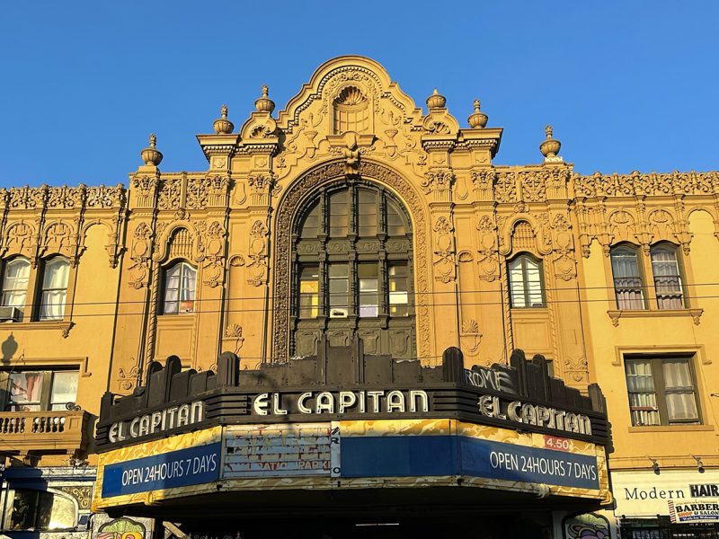 An ornate building facade with "El Capitan" signage and a marquee that reads "OPEN 24 HOURS 7 DAYS." The exterior displays intricate architectural details and multiple windows.