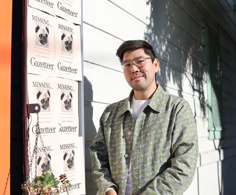 A person stands by a wall with missing dog posters, wearing glasses and a patterned jacket.