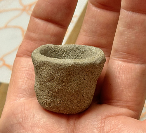 A person holds a small, textured clay pot in their hand.