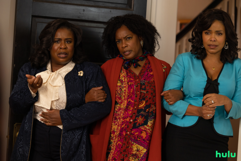 Three women stand indoors with concerned expressions, with one woman in a white blouse, another in a red patterned shawl, and the third in a teal top. Hulu logo is visible in the bottom right corner.