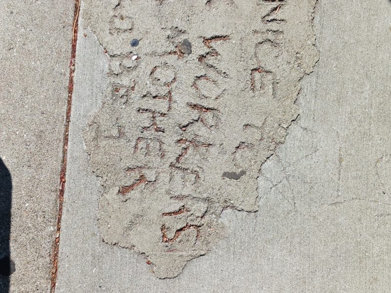Roughly carved text in concrete on a sidewalk reads: "BE NICE TO SEX WORKERS, YOUR MOTHER COULD BE 1."