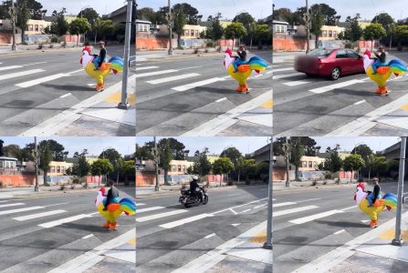 A person in a colorful rooster costume crosses the street at a crosswalk as a red car and a motorcyclist pass by.