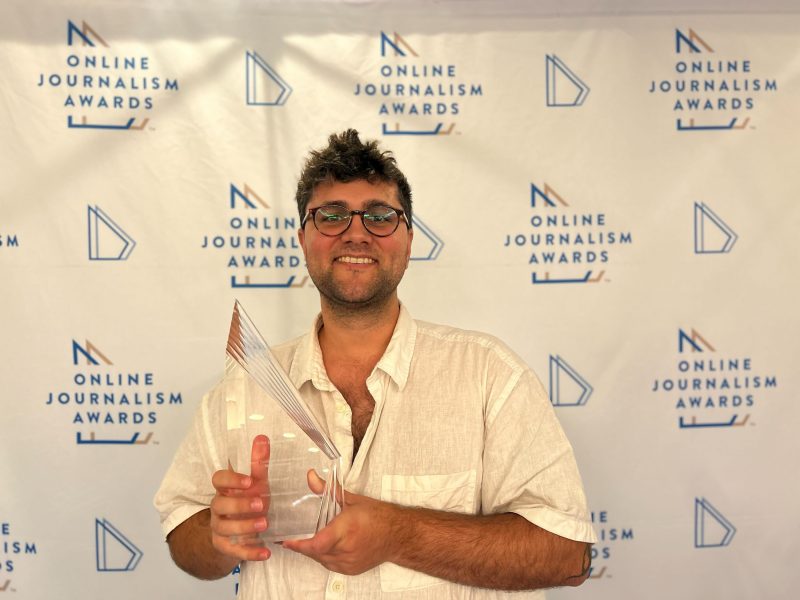 A person holding an award while standing in front of a backdrop that reads "Online Journalism Awards.