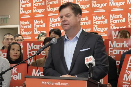 A man in a suit stands at a podium with "Mark Farrell for Mayor" signs in the background and people holding similar signs around him.