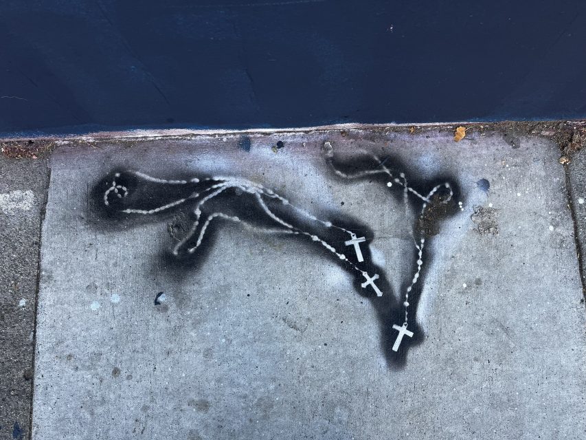 Graffiti of two white crosses connected by a line, spray-painted on a concrete sidewalk.
