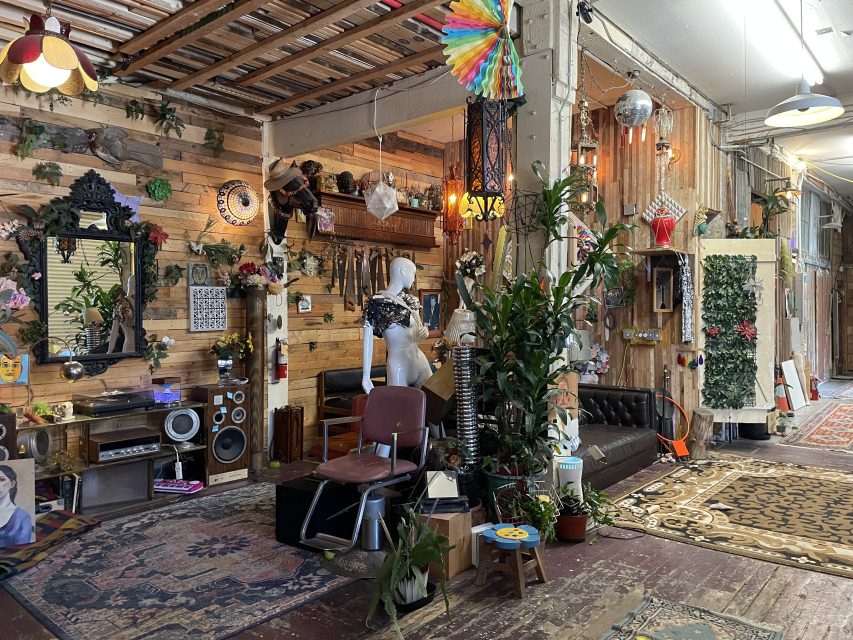 A room filled with eclectic decor, including plants, mirrors, a mannequin, furniture, wall hangings, and various ornaments, creating a bohemian and artistic atmosphere.