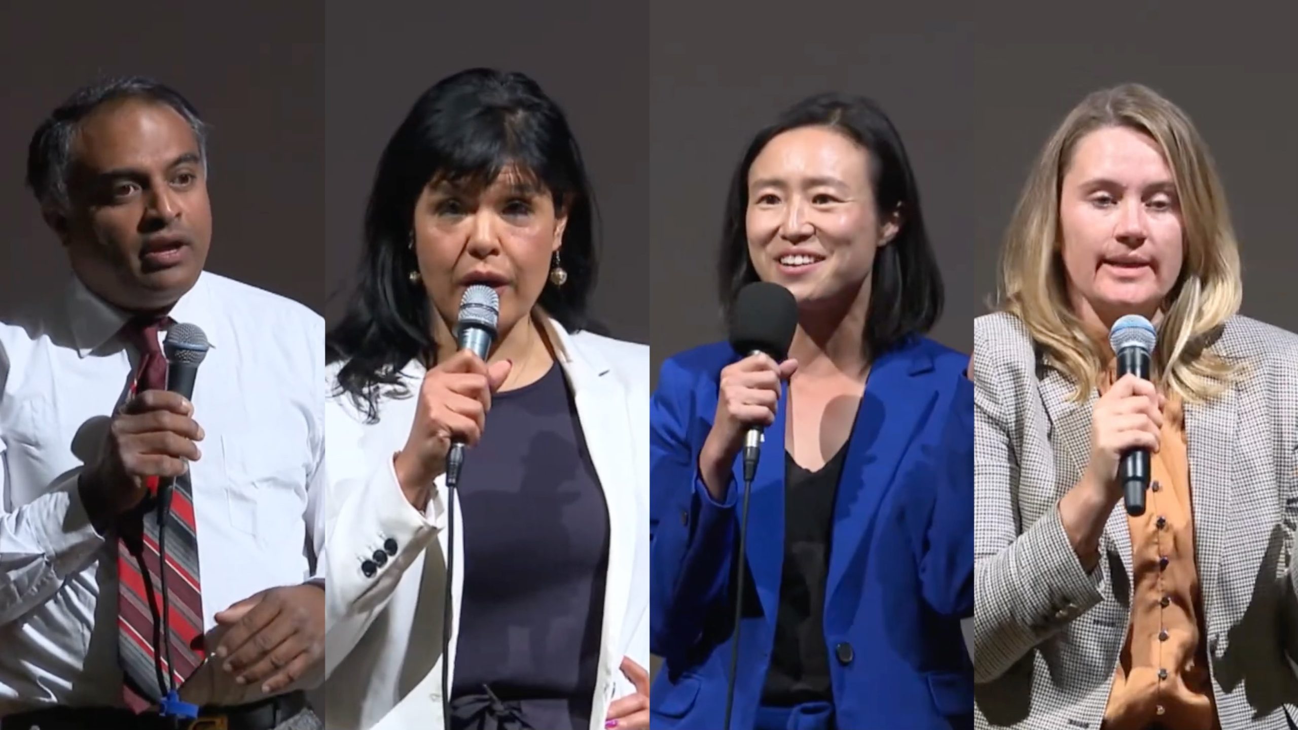 Four individuals stand side-by-side, each holding microphones and speaking. They are dressed in business attire and positioned against a plain backdrop.