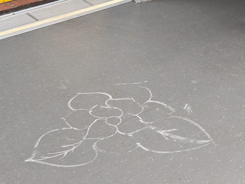 A chalk drawing of a flower with leaves is on the floor near an open train door.