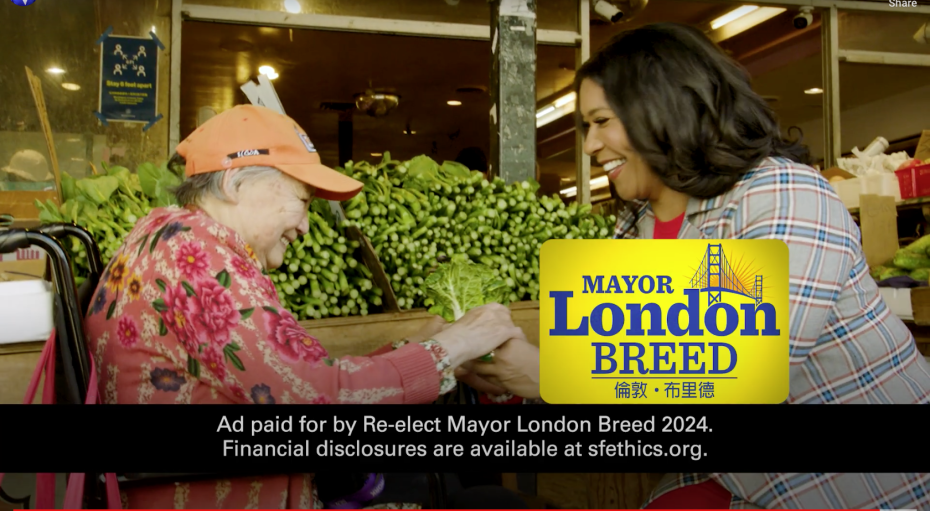 一位年長婦女和一位穿著格子夾克的女士在市場環境中微笑互動。展示著支持市長倫敦·布裡德連任競選的標牌。